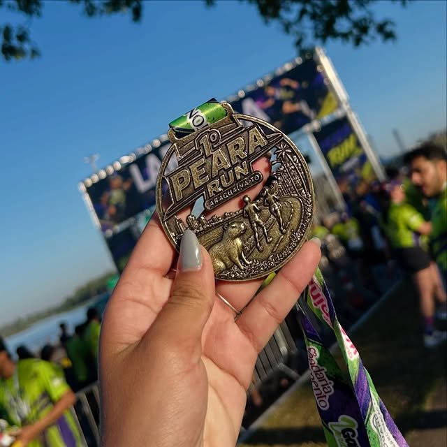 Close da medalha da Peara Run com a capivara em relevo, segurada em frente à estrutura do evento