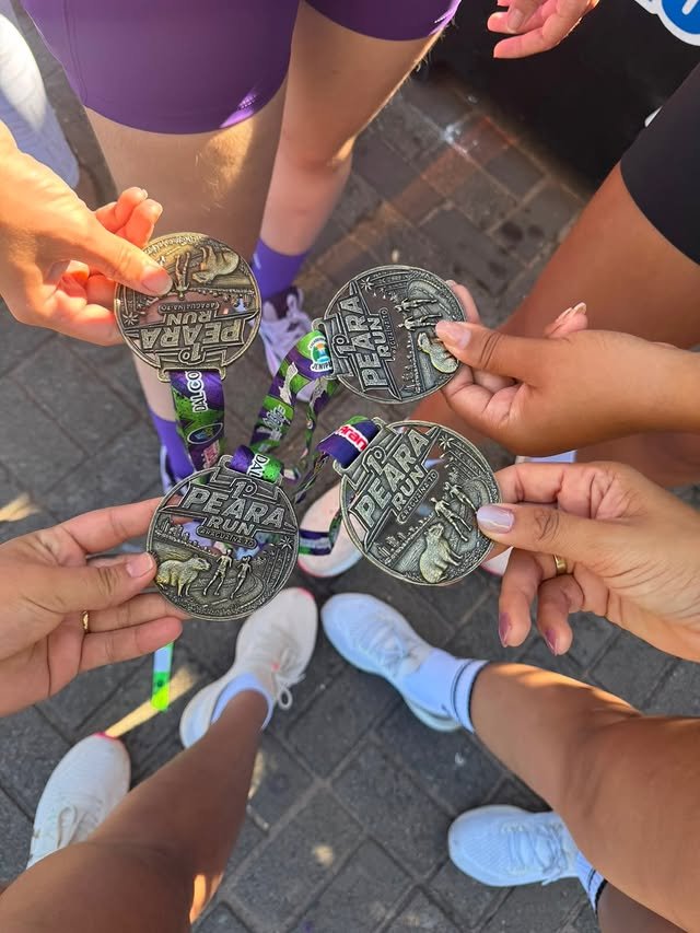 Quatro corredoras reúnem as medalhas da Peara Run no centro, mostrando o design exclusivo da prova